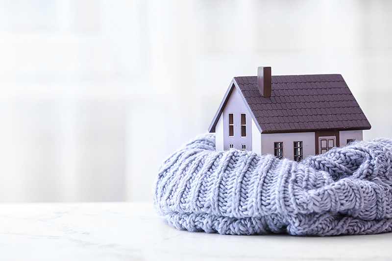 Wärmedämmwerte im Fokus – Symbolbild mit in Schal eingewickeltem Haus für Wärmedämmung